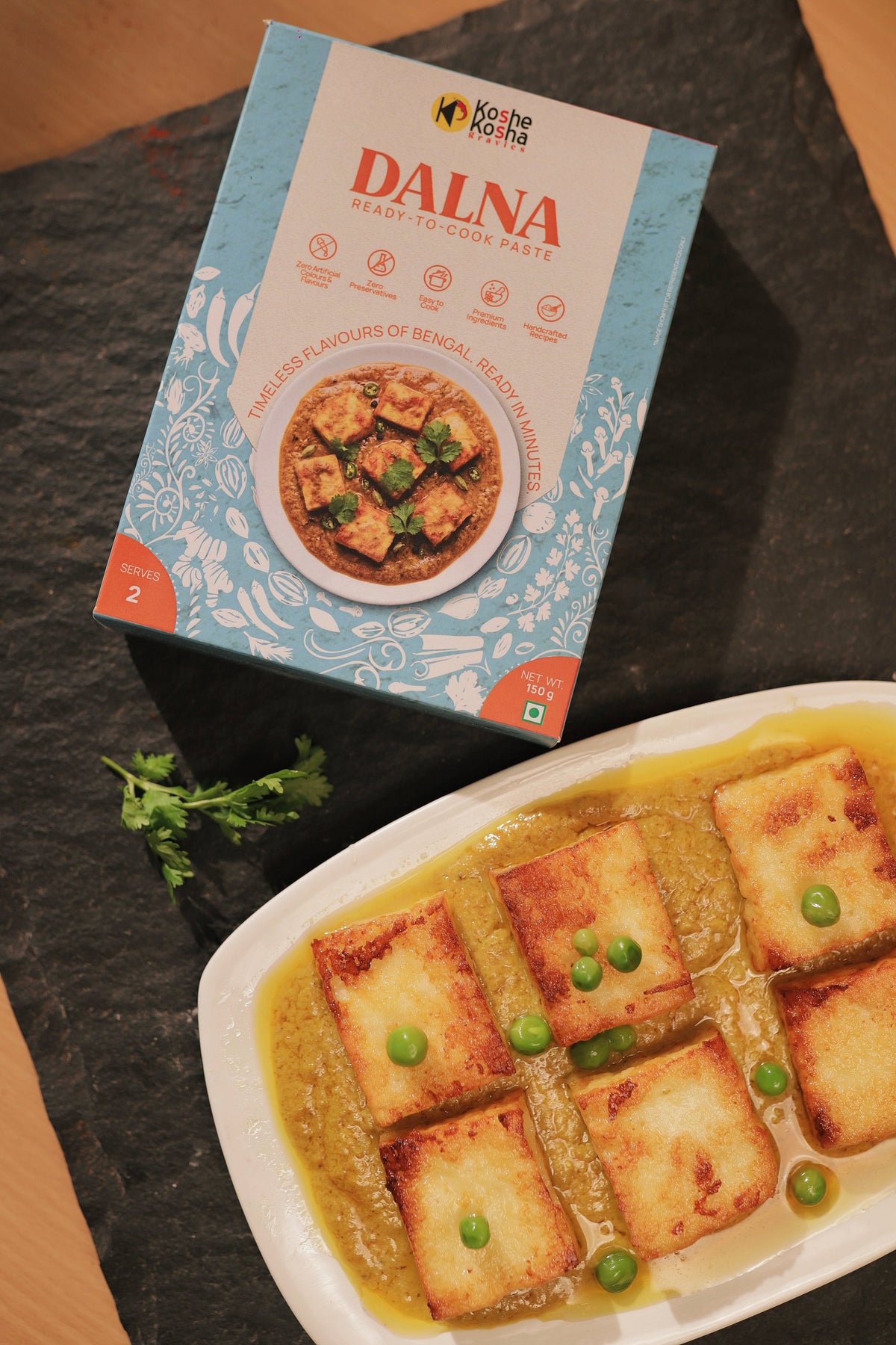 Dalna paste box on slate above a plate of fried chhana squares with green peas in dalna gravy