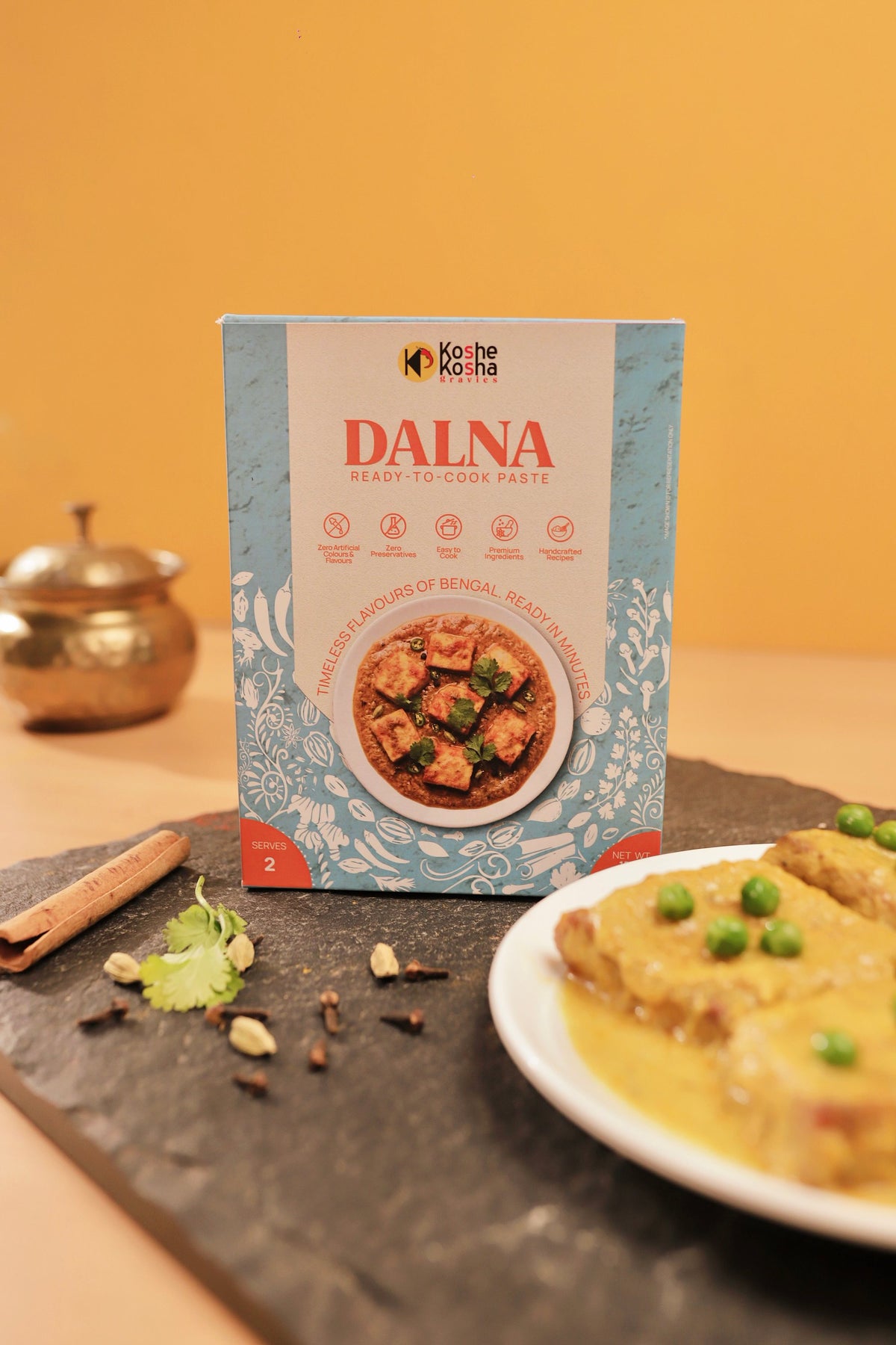 Dalna box with chhanar dalna and green peas on slate against a yellow wall