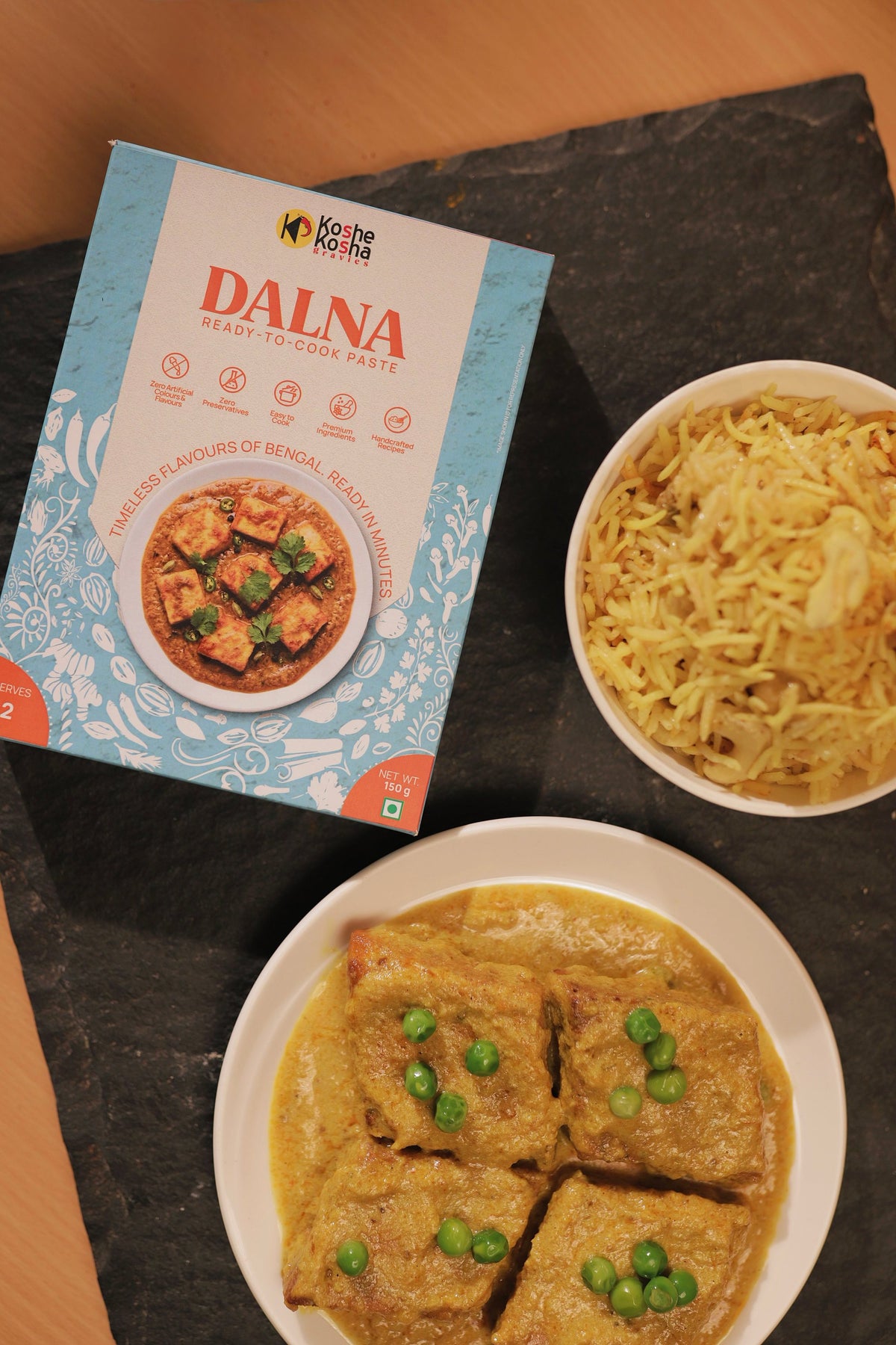 Top-down view of the Dalna box on slate with chhana dalna and a bowl of pulao
