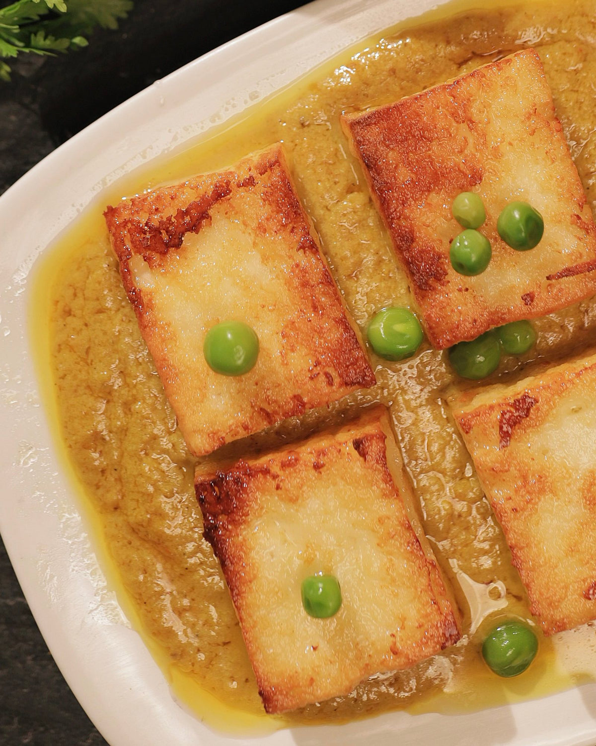 Close-up of fried chhana squares and green peas in dalna gravy