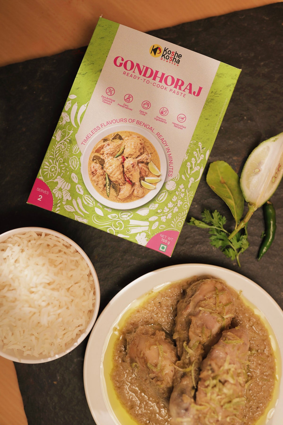 Gondhoraj paste box on slate with chicken in pale gondhoraj gravy, steamed rice, a halved lemon and green chillies