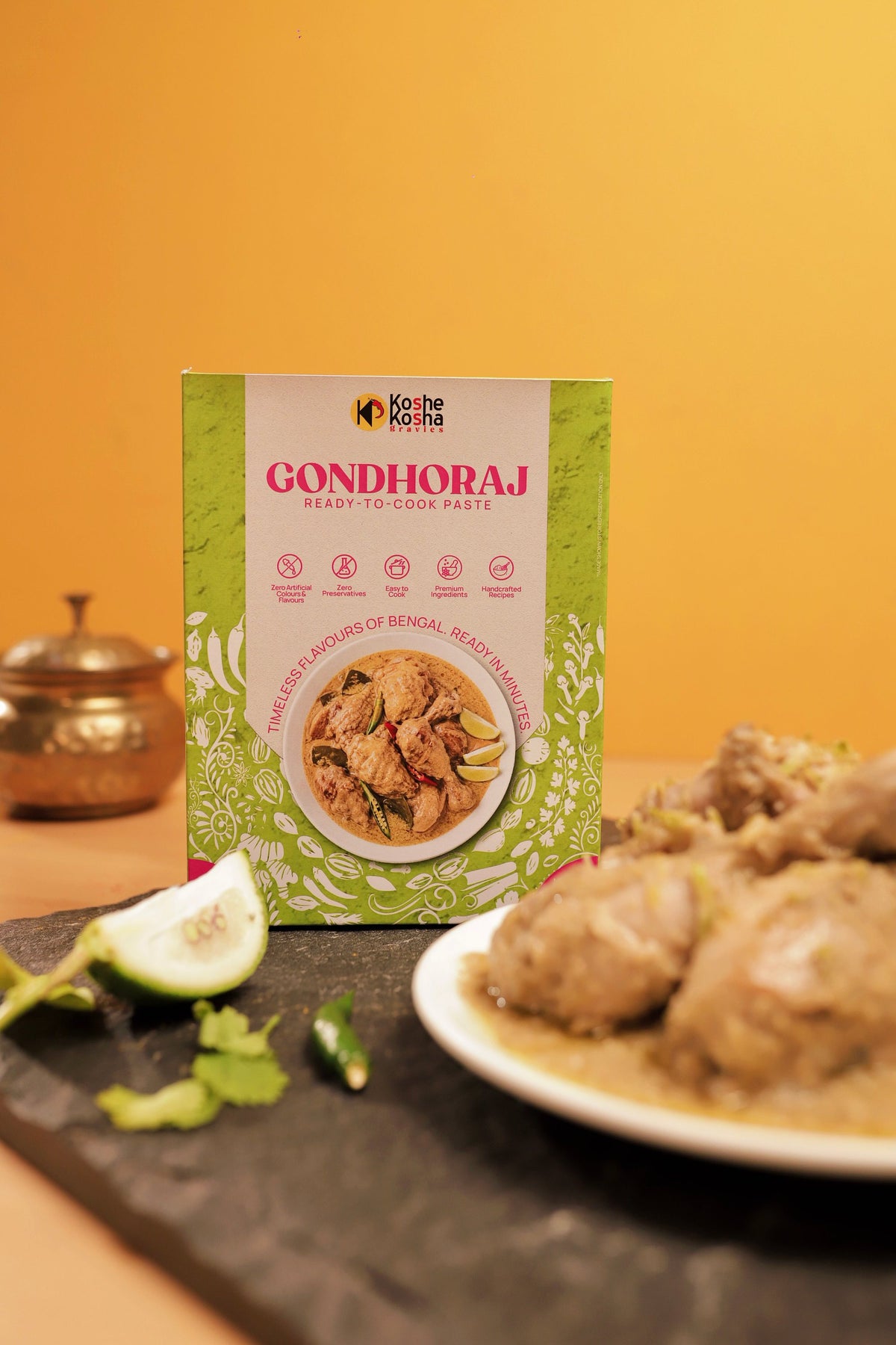 Gondhoraj box with a plate of gondhoraj chicken and a lemon wedge against a yellow wall