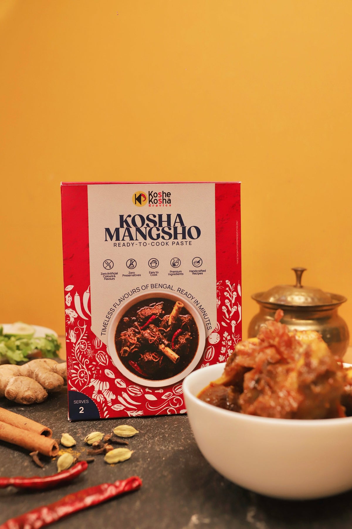 Kosha Mangsho box and a bowl of mutton kosha against a warm yellow wall