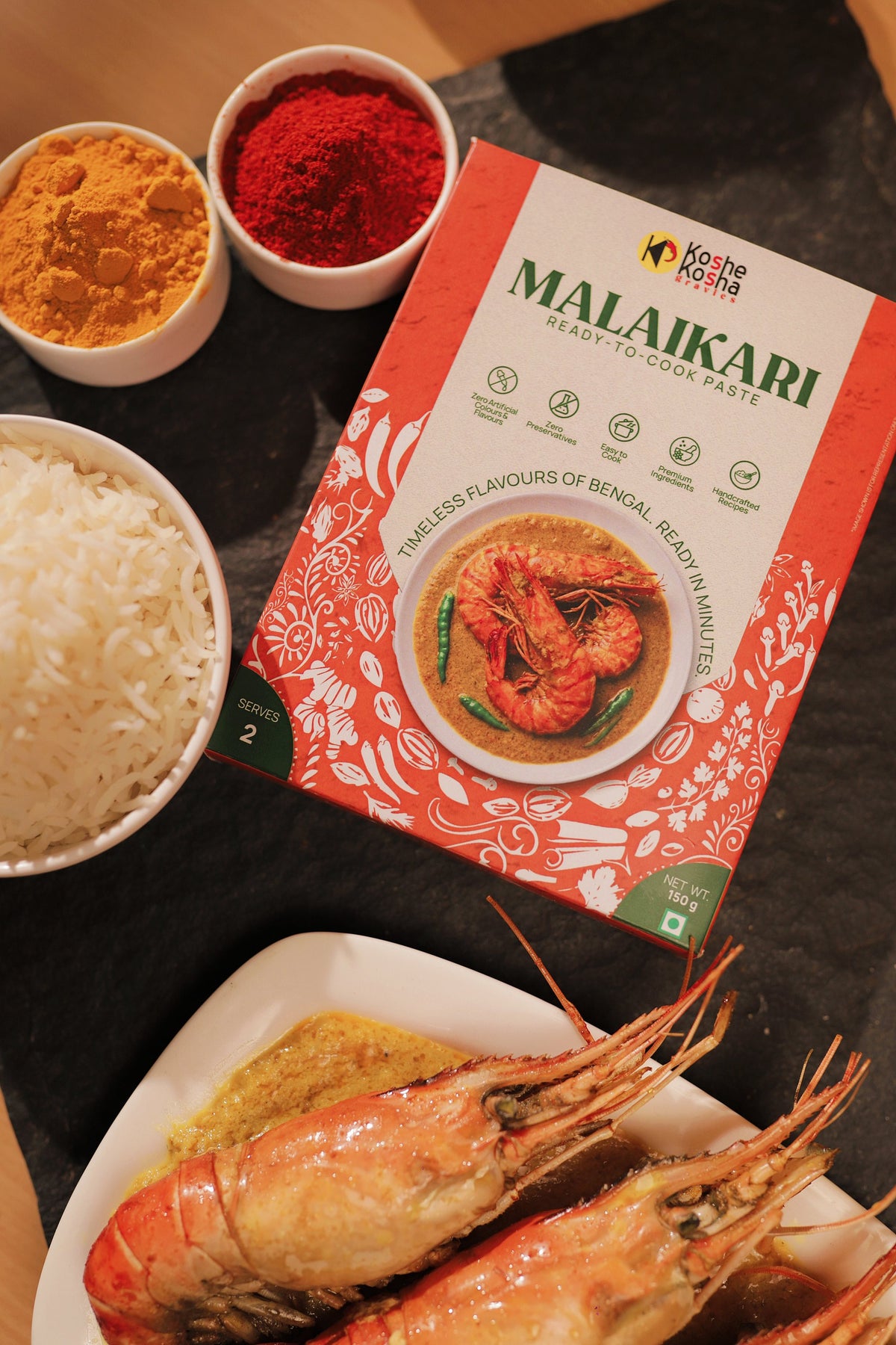 Malaikari paste box on slate with whole prawns in creamy malaikari gravy, steamed rice, and bowls of turmeric and chilli powder