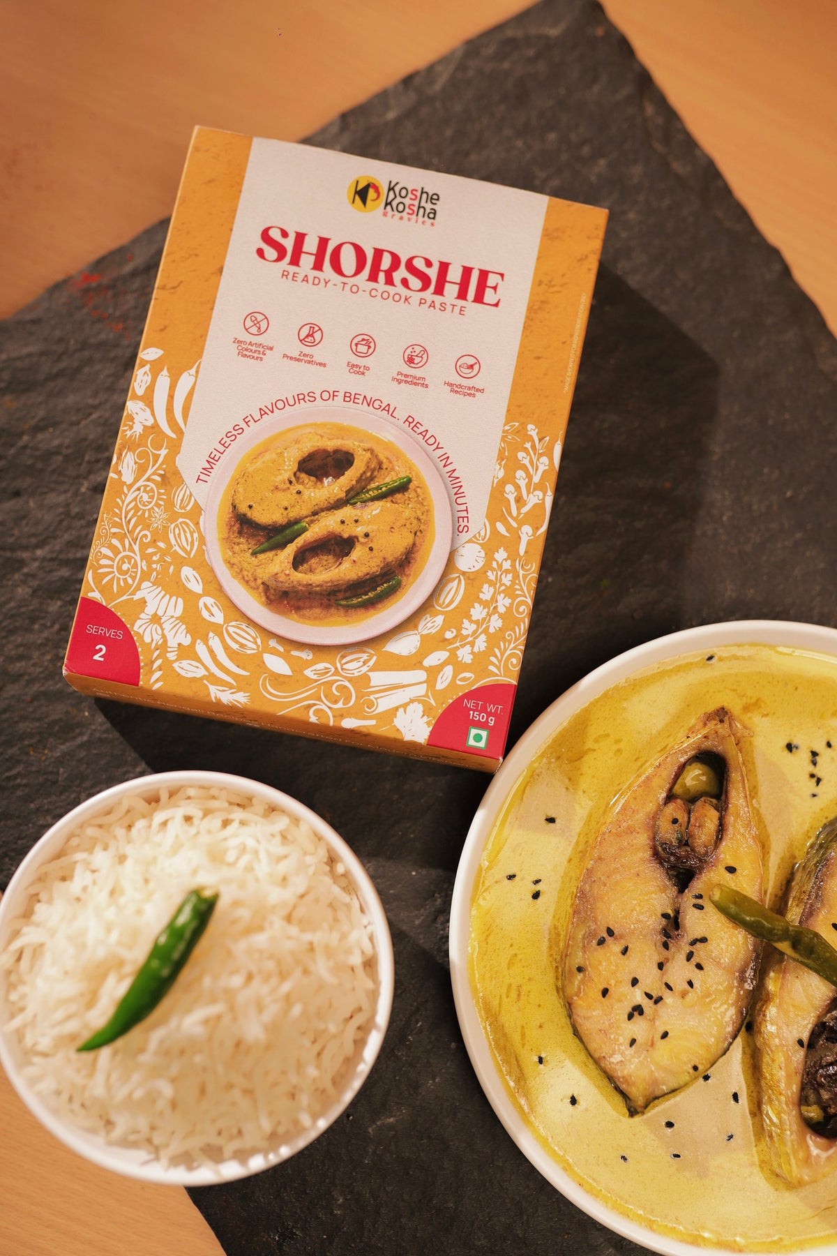 Shorshe paste box on slate with fish steaks in yellow mustard gravy and a bowl of rice with a green chilli