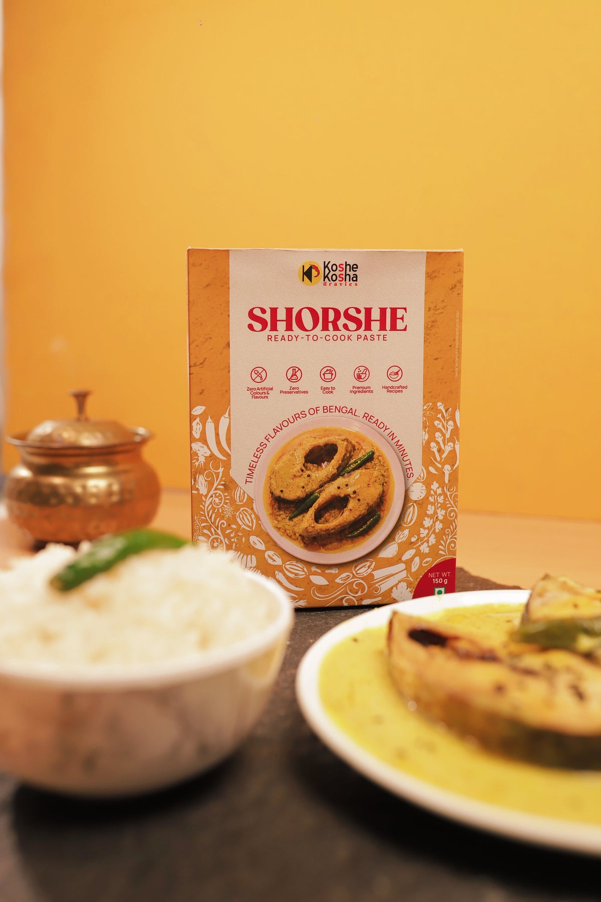 Shorshe box with fish in mustard gravy and rice against a yellow wall
