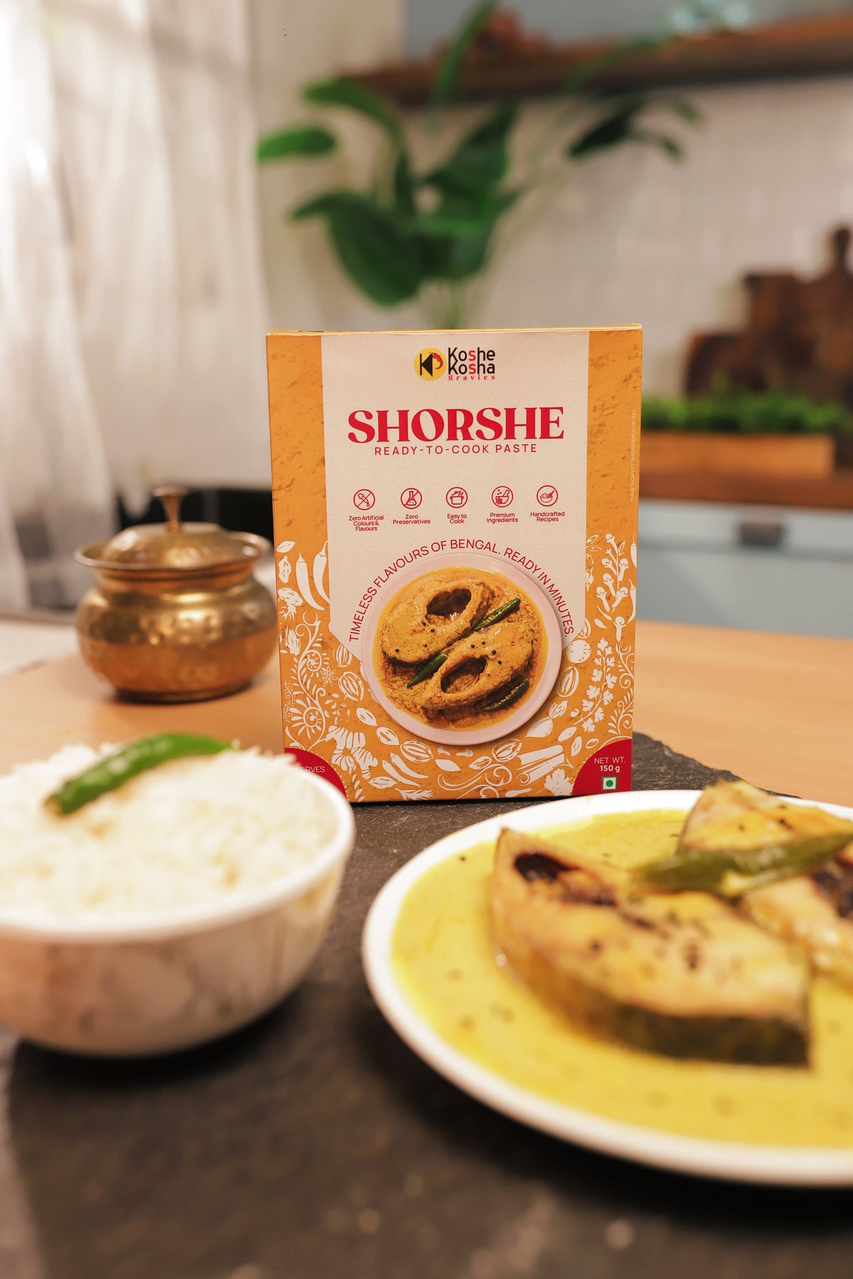 Shorshe box with shorshe fish, rice and a green chilli in a home kitchen