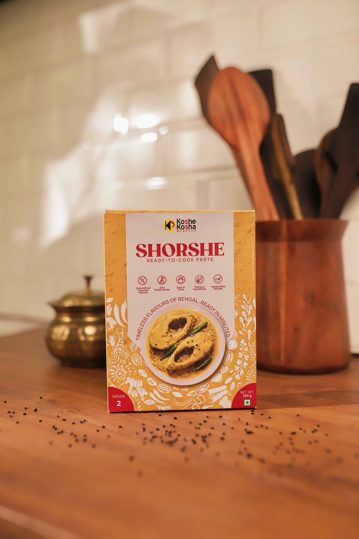 Shorshe box on a wooden counter with scattered mustard seeds and wooden spoons