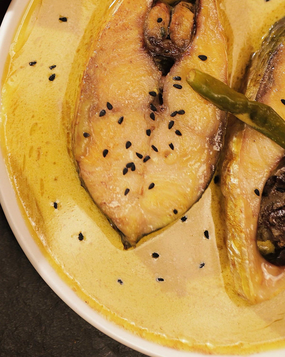 Close-up of fish steaks in yellow mustard gravy with a green chilli