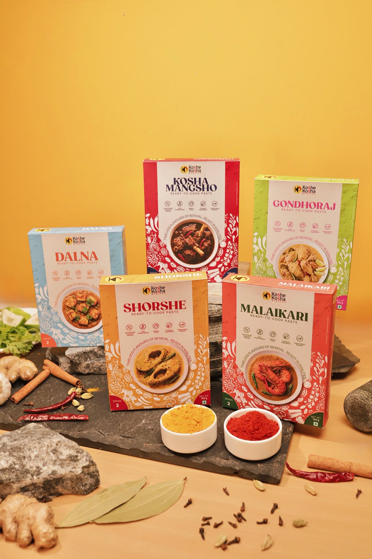 The five paste boxes on slate with ginger, bay leaves and whole spices against a yellow wall